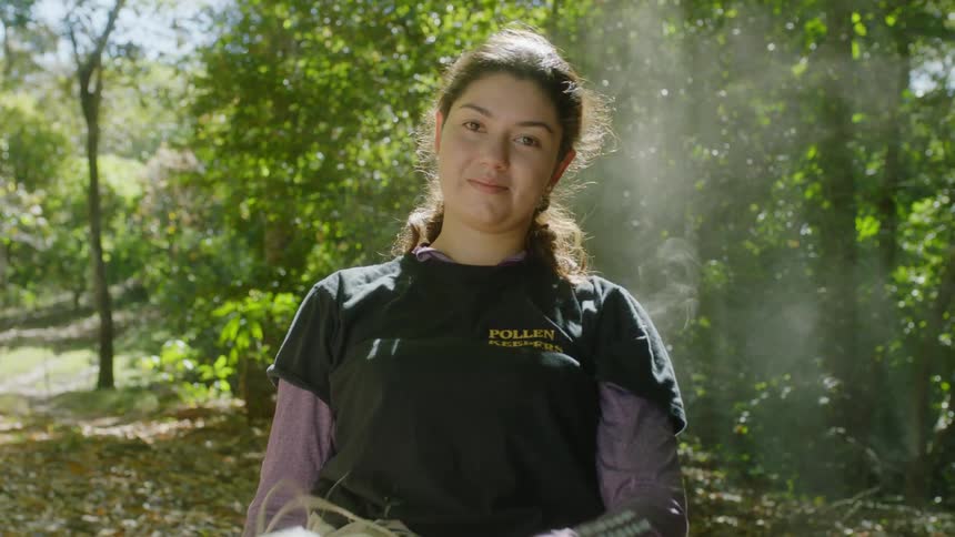 Female beekeeper wearing apiary related shirt removes meshed headgear