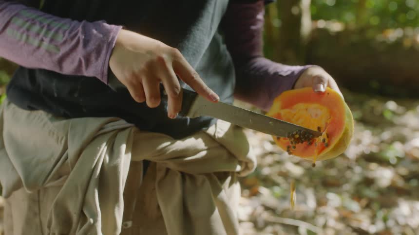 A person is picking the seeds out of a fruit with a knife