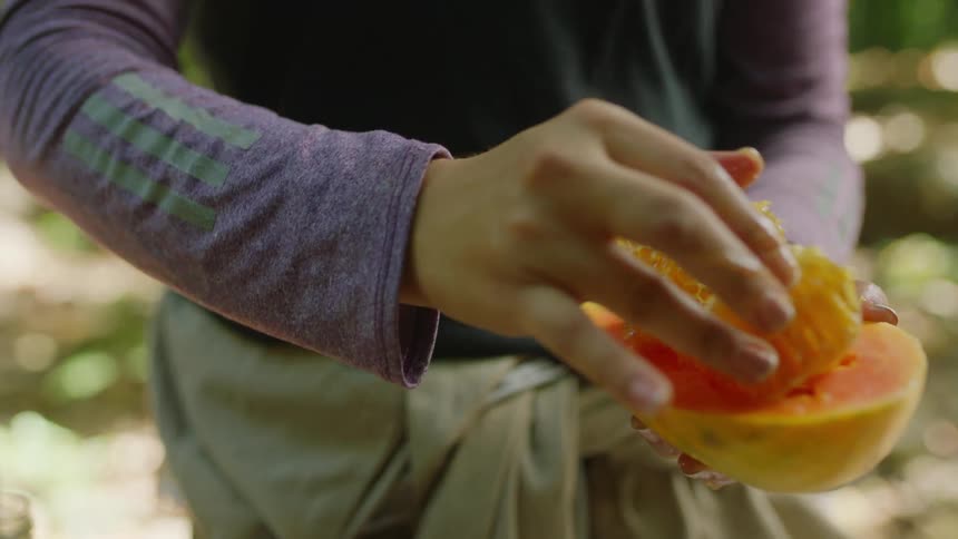 Closeup of woman placing honeycomb chunks on a fresh papaya half