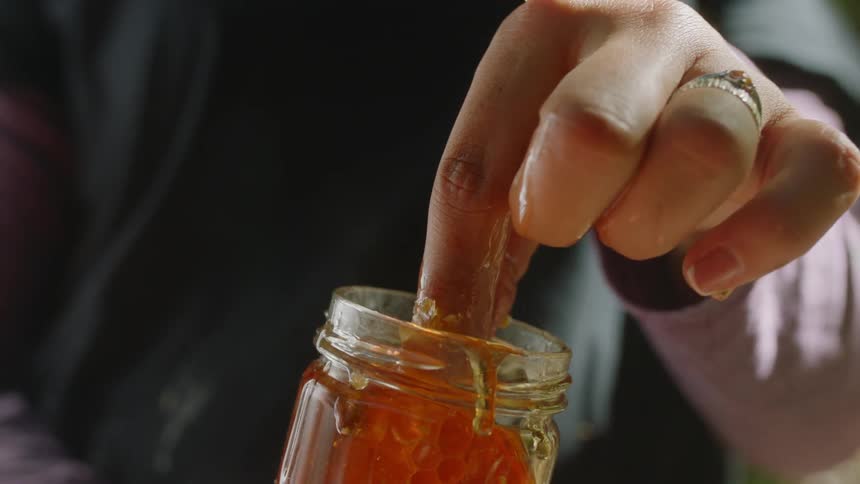 Female hand pulling out a large honeycomb from glass honey jar