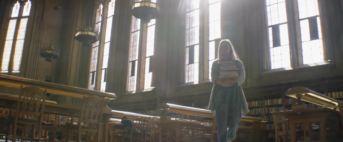 Woman carries a stack of books through a library
