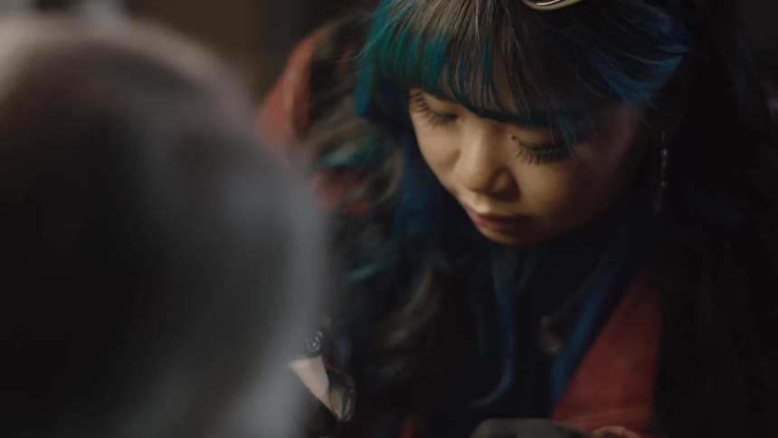 Young female tattoo artist with colorful hair wearing black latex gloves drawing on a clients forearm