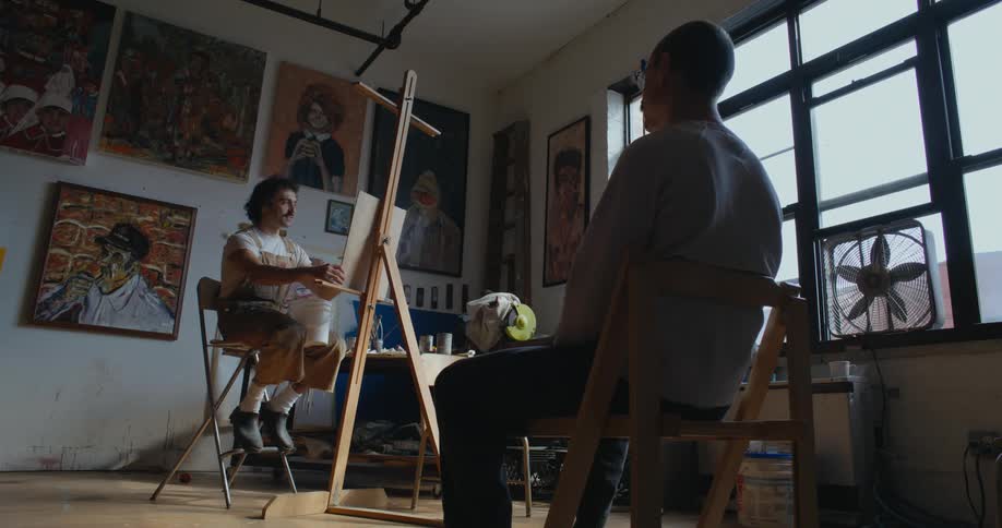 A man sits in a chair in front of an artist as he paints him