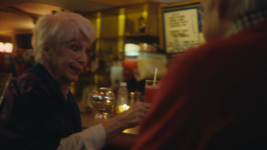 Happy elderly couple on a date sit on a bar drinking cocktails