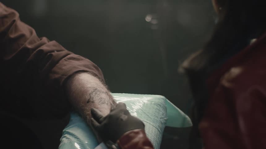 Female tattoo artist puts tattoo on elderly mans arm using a tattoo gun