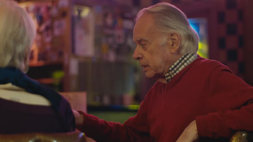 An elderly man and woman sit at a bar counter and talk