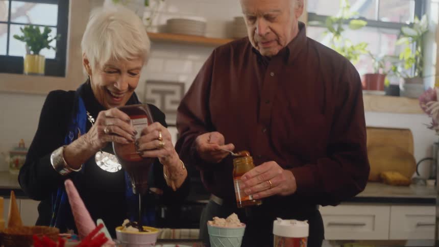 A man and woman put toppings on their ice cream