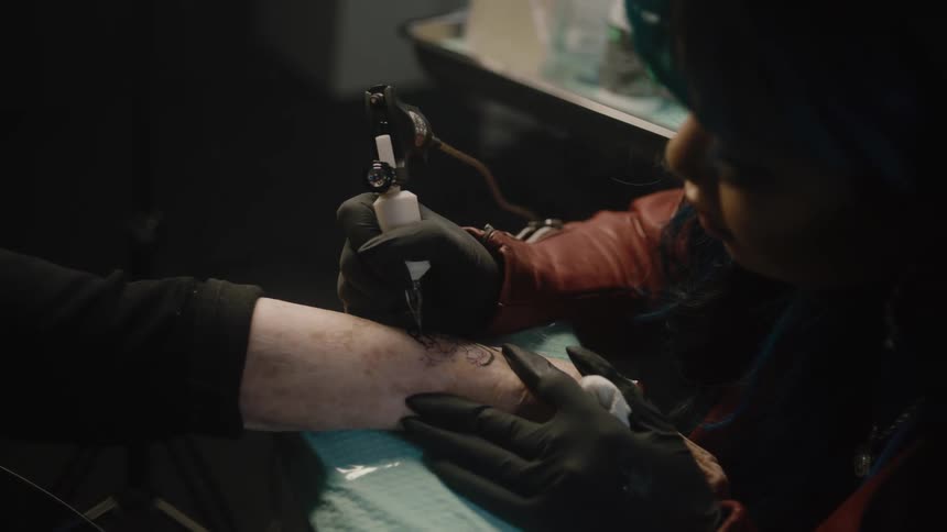 Female tattoo artist tattoos clients forearm