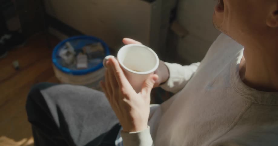 A man is sitting indoors and drinking a cup of coffee