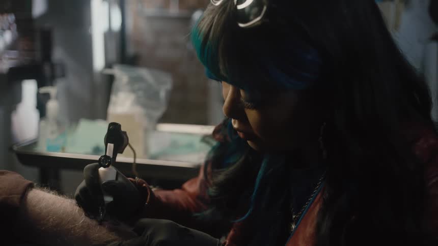 Female tattoo artist uses a needle and ink to apply a tattoo onto the arm of an elderly man