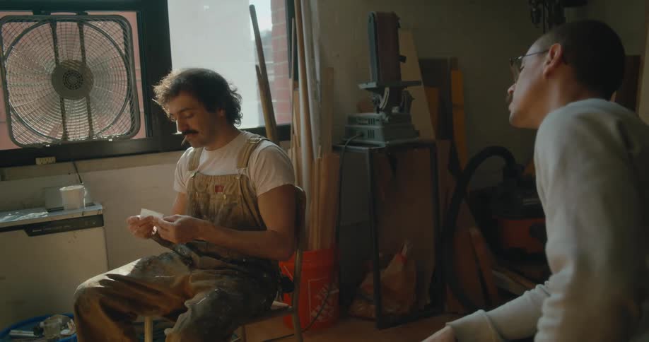 One man sits watching another who is wearing overalls