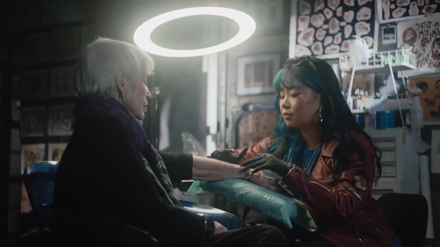 A tattoo artist gives a tattoo to an elderly woman