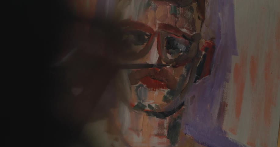 An artist paints a picture of a man wearing glasses on a canvas