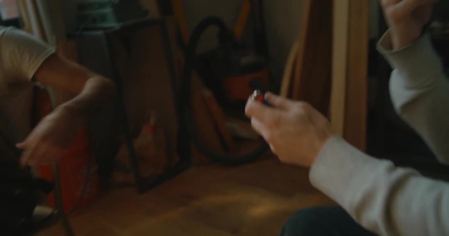 A man twists the end of a cigarette and then another man hands him a lighter and he lights his cigarette and smokes