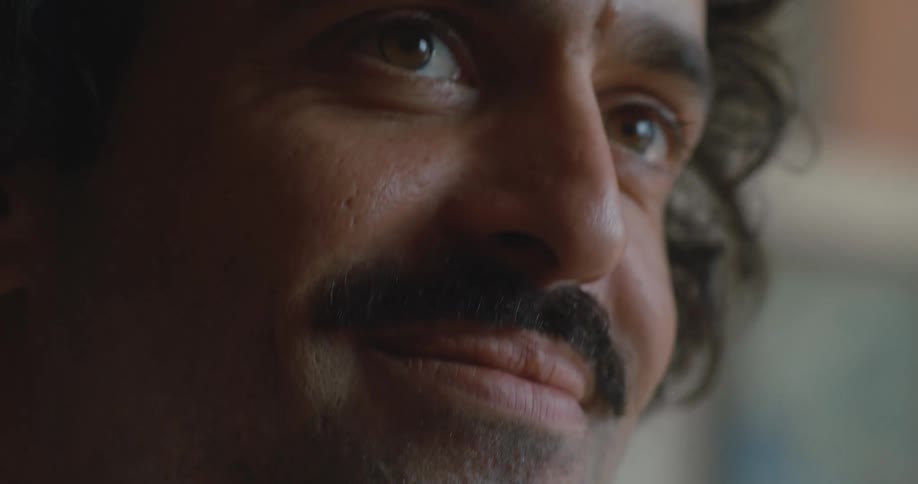 A man is smiling and sitting indoors during the daytime