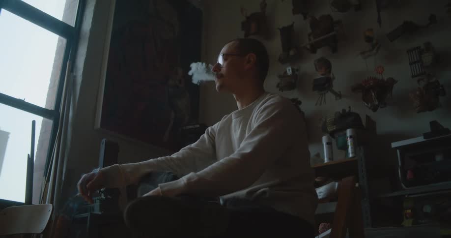Man sits in room near window smoking a cigarette