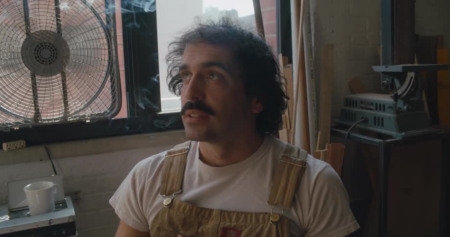 A man is sitting indoors and smoking a cigarette near a window