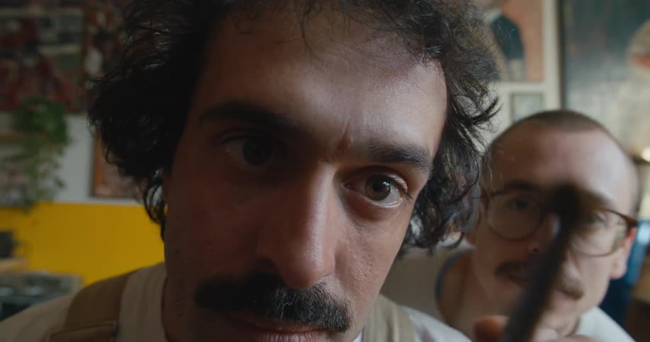 Close up of a mans face as he uses a paint brush and another man is looking over his shoulder