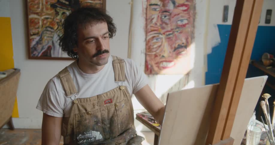 An artist paints on a canvas in a studio