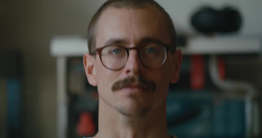 A man sits with no expression on his face and then nods his head and smiles
