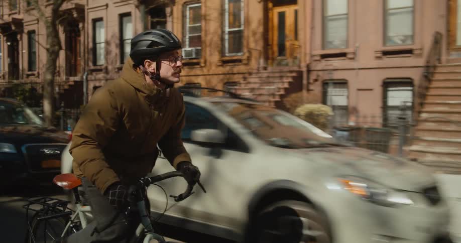 A man is biking on a street through a suburban city