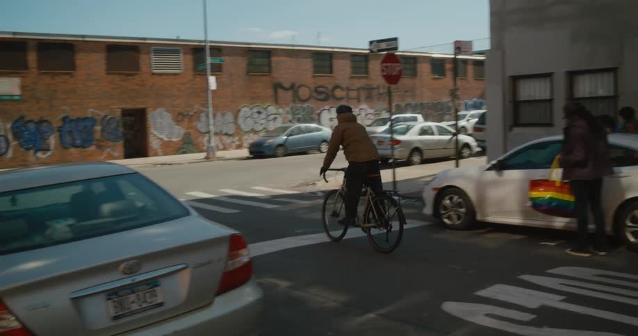 A man rides his bicycle on a street passing parked cars and buildings