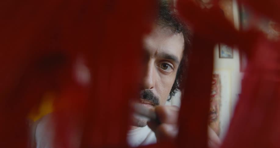 View through glass of a man painting on it with red paint until it is covered