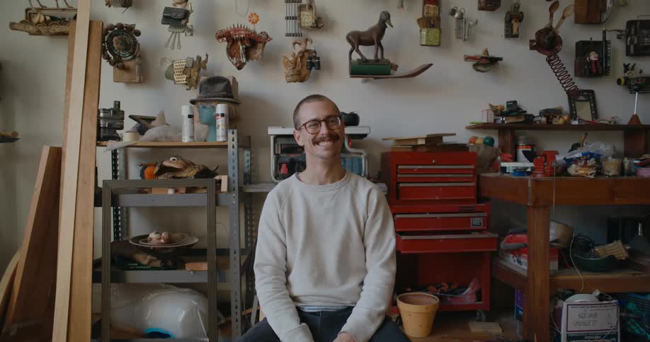 Man poses in workshop with modern art sculpture models in the background