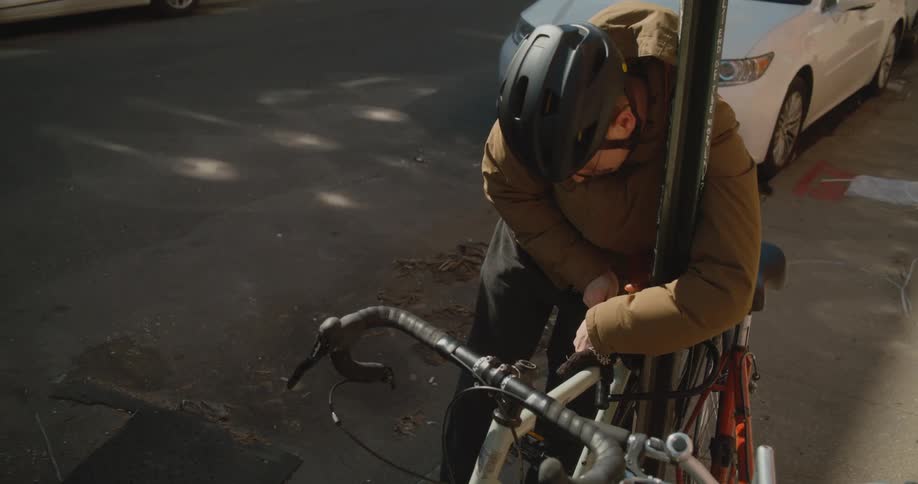 Man attaches bicycle to pole with bike lock as pedestrians walk by