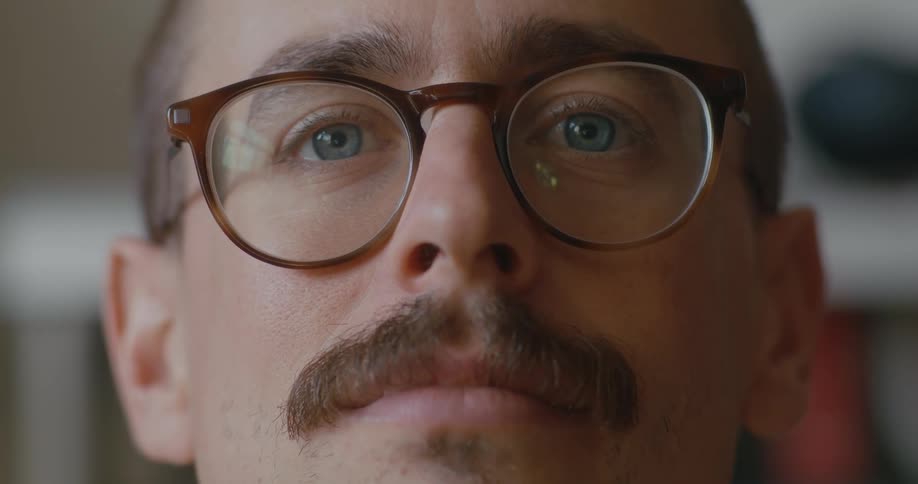 A man wearing glasses turns his head to look into the camera for a moment before smiling