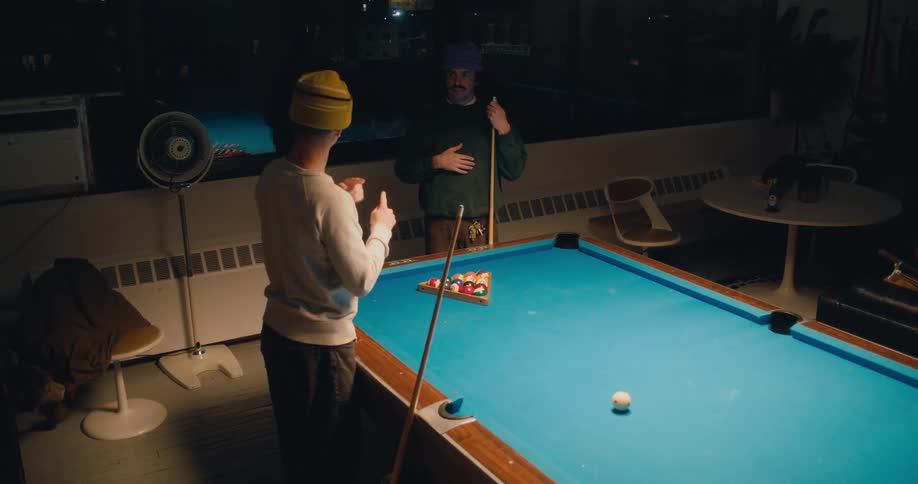 Two men are playing pool together indoors and talking with sign language