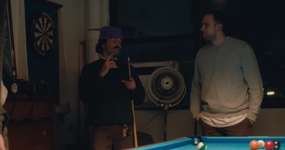 Men stand in game room near pool table and windows showing night sky as they converse with sign language