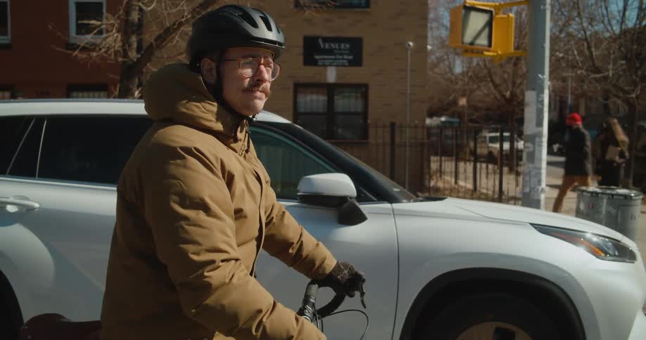 Pedestrians walk along sidewalk as cyclist and car wait at intersection