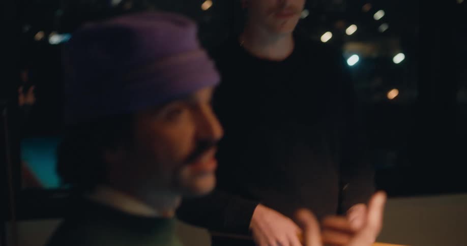 Men converse using sign language while playing pool as city light can be seen through window in the background