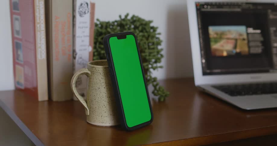 A smartphone kept vertical by leaning against a coffee mug on a desk