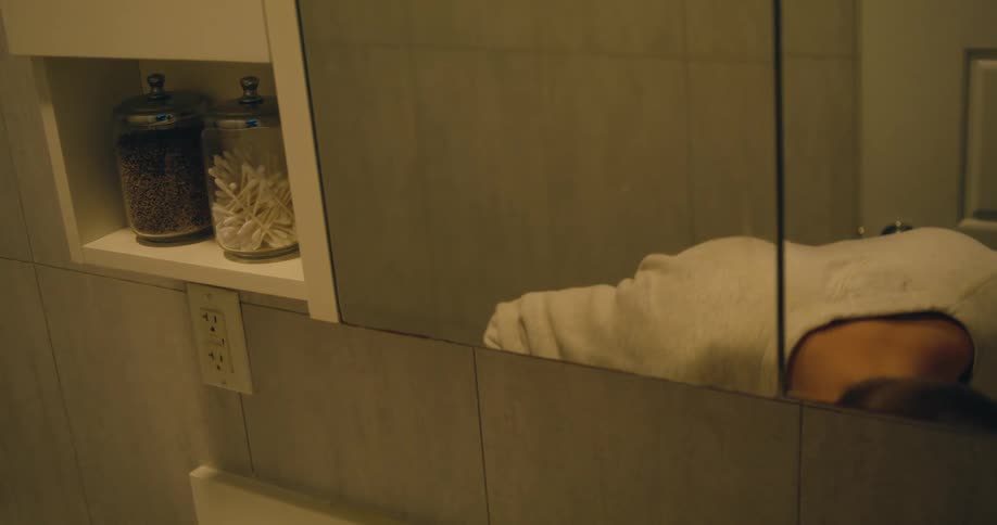 Man with glasses and gray sweatshirt brushes his teeth using electric toothbrush in the bathroom