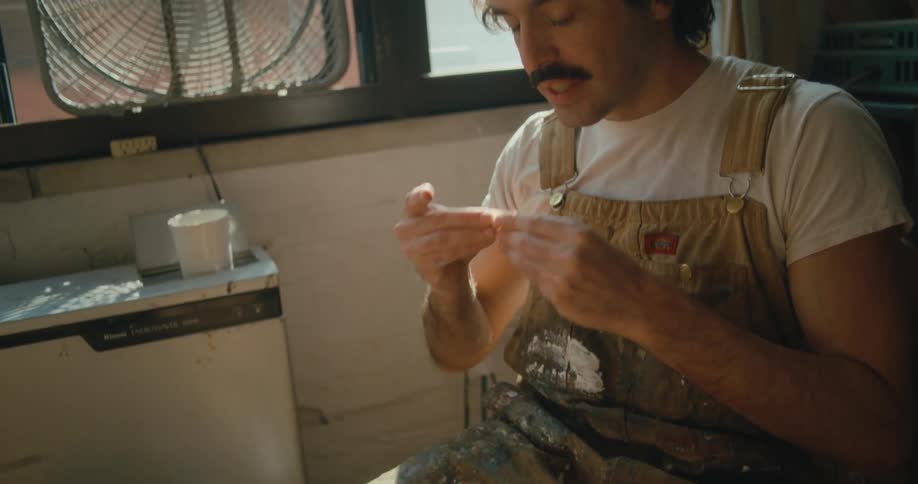 Man with a mustache rolls then licks cigarette paper and then passes it over to another person