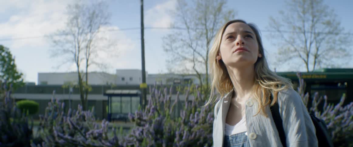 A woman turns from some flowers to look up at the sky