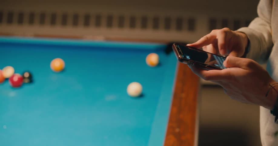 Friends playing pool at night help each other to compose a text message on a phone