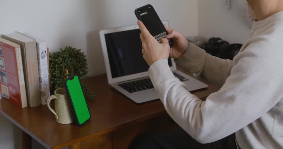 A man is sitting near a laptop and texting on a cellphone