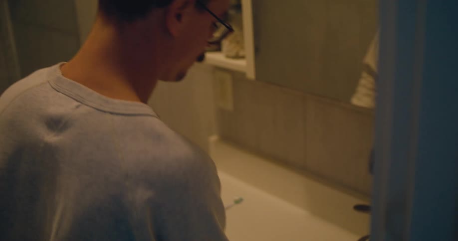 A man at home gets his toothbrush out rubs his beard and brushes his teeth