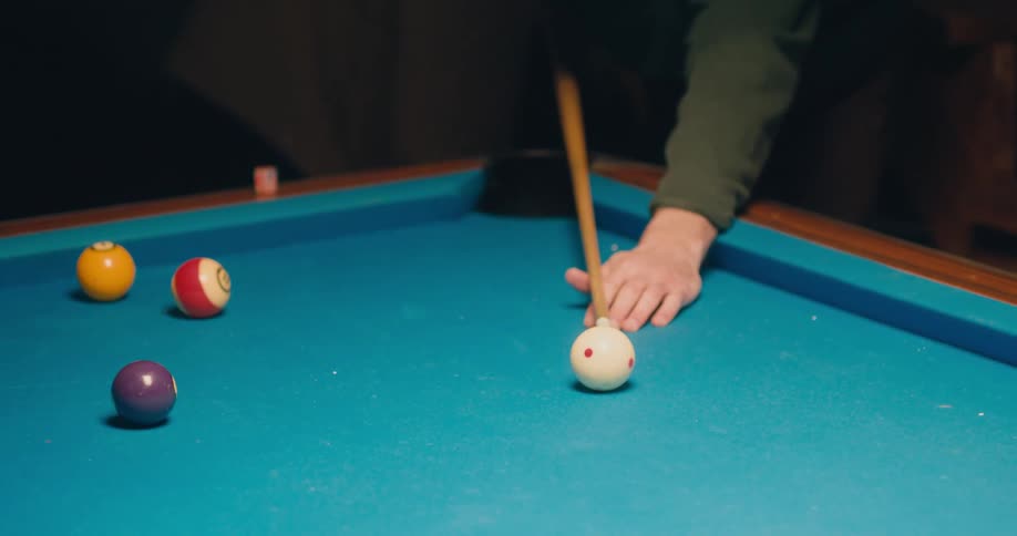 A man talks to someone and then takes a shot while playing pool