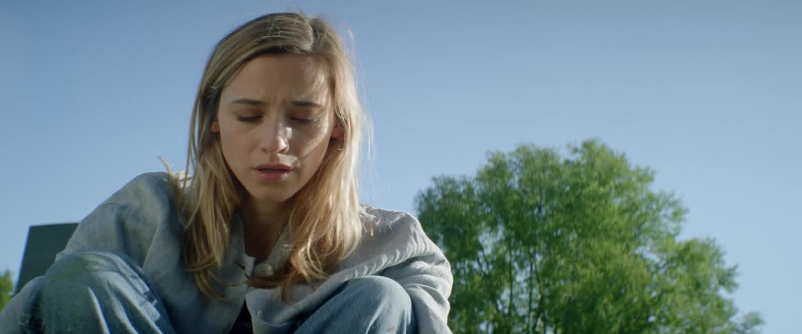 A woman is sitting outside on a sunny day looking sad