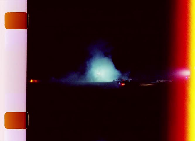 Race cars driving at night caught on vintage film