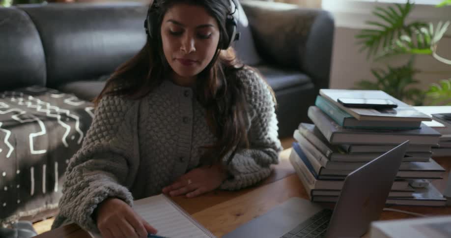 A woman wearing headphones writes and plays the keyboard