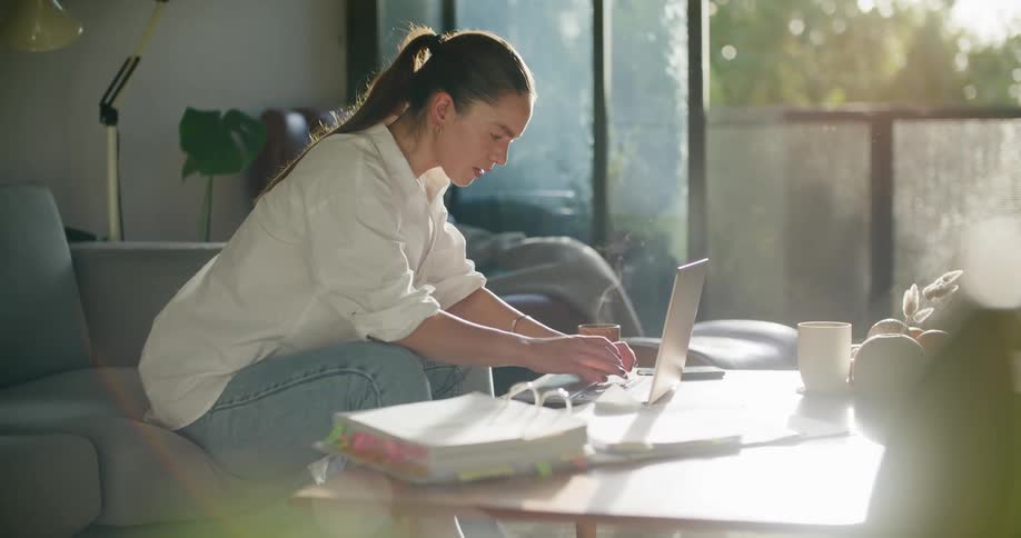 A female looks at notes in a binder and then begins to type on the laptop in front of her