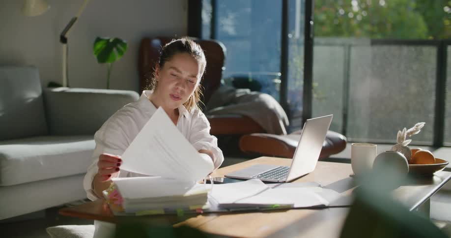 A hispanic woman reads notes while talking with someone on the laptop in front of her