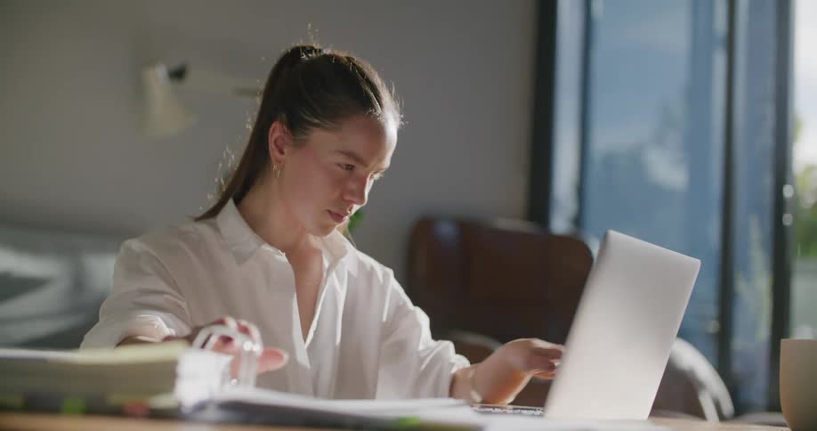 Woman works on laptop in living room after consulting binder