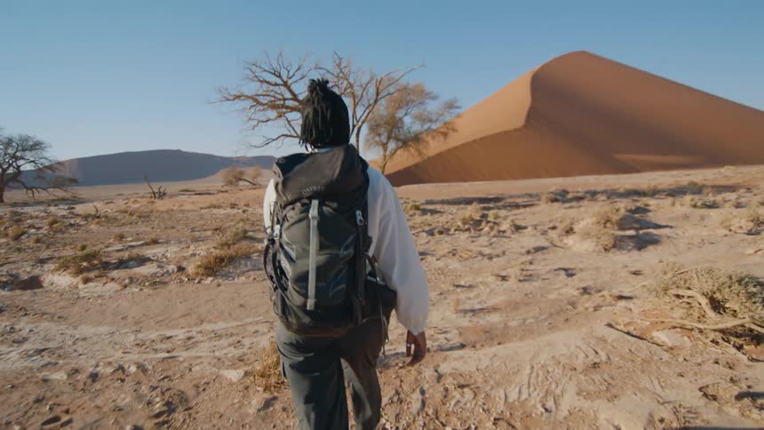 Woman with dreadlocks white shirt green pants and shoes walks across the desert