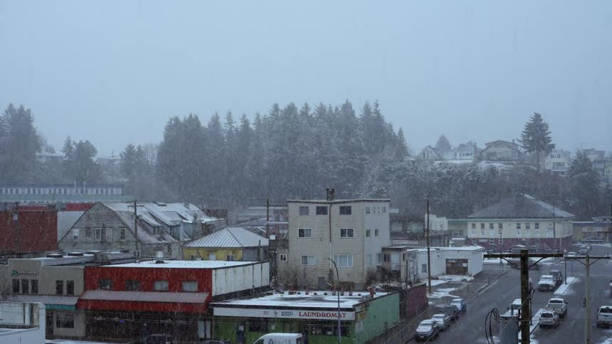 Snow falls from sky on town with buildings and roads
